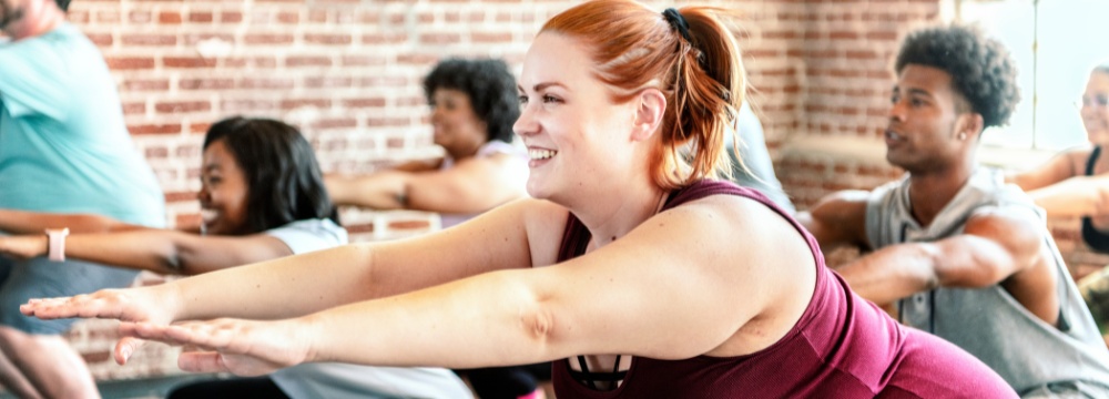 Woman in excercise class doing a squat with hands infront of her while smiling 