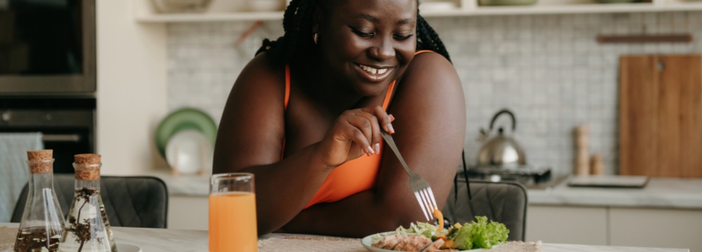 Woman leaning on kitchen island while eating salad with fork 